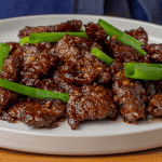 P.F. Chang's Mongolian Beef with dark sauce and green onions on a white plate
