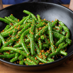 Din Tai Fung green beans with garlic served on a plate with visible blistered skins and bits of zha cai