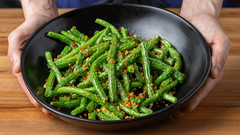 Din Tai Fung green beans with garlic served on a plate with visible blistered skins and bits of zha cai