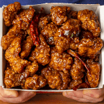 general tso's chicken in a takeout container with crispy coating and glossy sauce