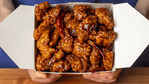 general tso's chicken in a takeout container with crispy coating and glossy sauce