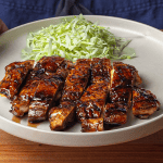 Sliced Japanese teriyaki chicken thighs glazed with tare sauce, served over short-grain rice with shredded cabbage