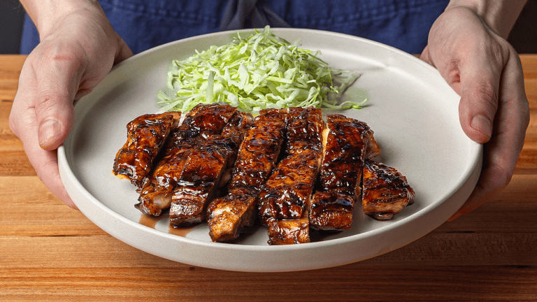 Sliced Japanese teriyaki chicken thighs glazed with tare sauce, served over short-grain rice with shredded cabbage