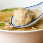 chinese takeout wonton soup in a bowl with translucent pork and shrimp wontons in clear broth