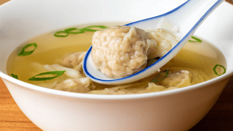 chinese takeout wonton soup in a bowl with translucent pork and shrimp wontons in clear broth