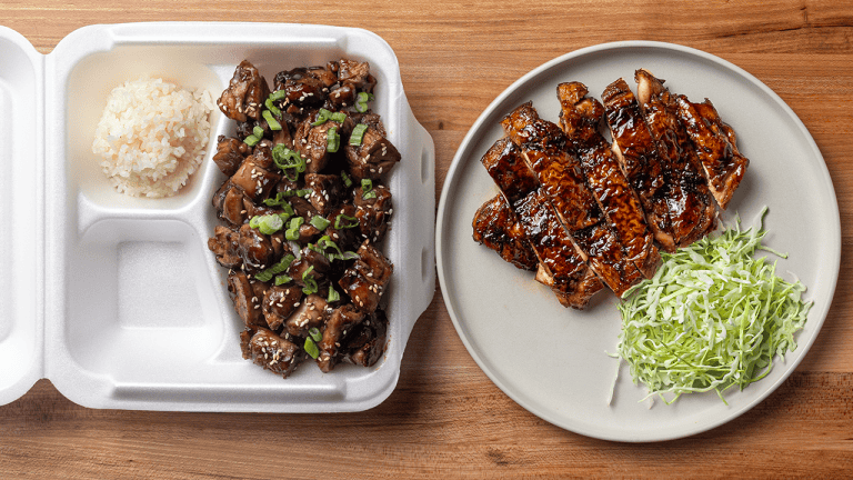 American teriyaki chicken served over white rice topped with sesame seeds and sliced scallions with japanese teriyaki on a white plate with shredded green cabbage