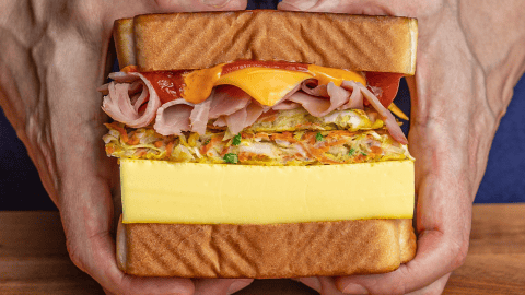Korean street toast cut diagonally showing steamed egg patty, cabbage fritter, ham, cheese, and sauces