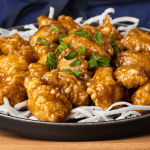 P.F. Chang's crispy honey chicken on fried rice sticks garnished with sliced green onion