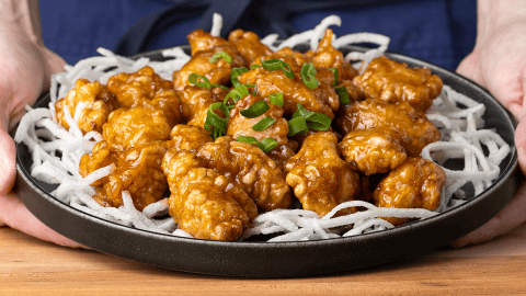 P.F. Chang's crispy honey chicken on fried rice sticks garnished with sliced green onion