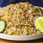 Thai fried rice served with cucumber slices lime wedges and crushed chili flakes