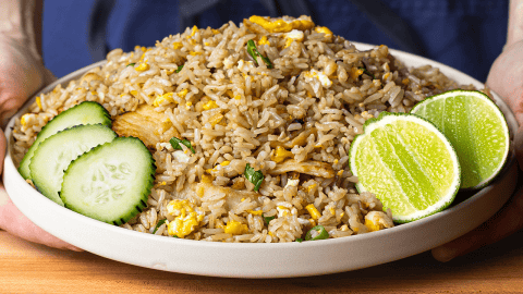 Thai fried rice served with cucumber slices lime wedges and crushed chili flakes