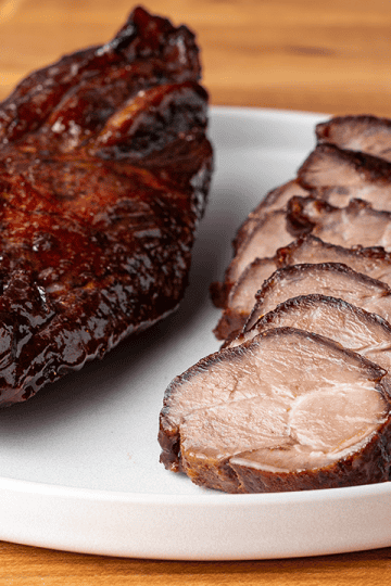 Sliced char siu Chinese BBQ pork with glossy maltose lacquer on a cutting board