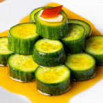 Din Tai Fung cucumber salad coins stacked in a pyramid with a garlic slice and Fresno chili on top and a clear red chili oil moat