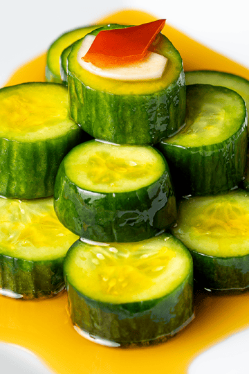 Din Tai Fung cucumber salad coins stacked in a pyramid with a garlic slice and Fresno chili on top and a clear red chili oil moat
