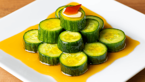 Din Tai Fung cucumber salad coins stacked in a pyramid with a garlic slice and Fresno chili on top and a clear red chili oil moat