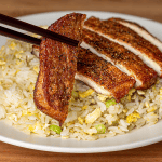 Sliced Din Tai Fung pork chop fried rice on a white plate, with chopsticks lifting one peppered slice of pork
