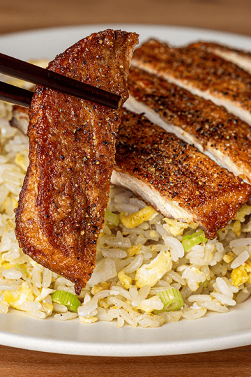 Sliced Din Tai Fung pork chop fried rice on a white plate, with chopsticks lifting one peppered slice of pork