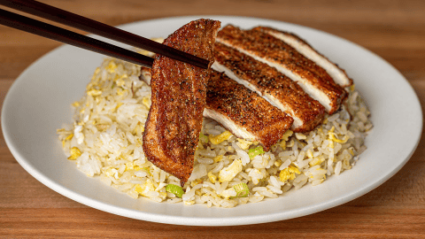Sliced Din Tai Fung pork chop fried rice on a white plate, with chopsticks lifting one peppered slice of pork