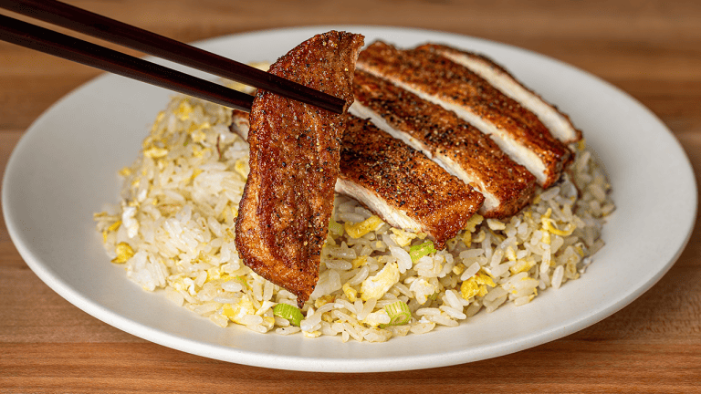 Sliced Din Tai Fung pork chop fried rice on a white plate, with chopsticks lifting one peppered slice of pork