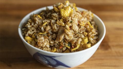 Benihana chicken fried rice with egg and sesame seeds in a white bowl with a blue pattern on a wooden table