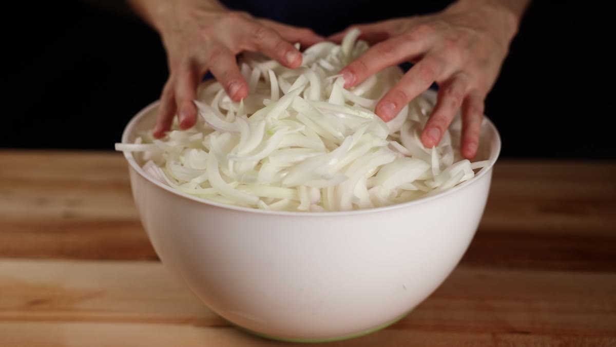 Hands resting on a big white bowl piled high with sliced onions