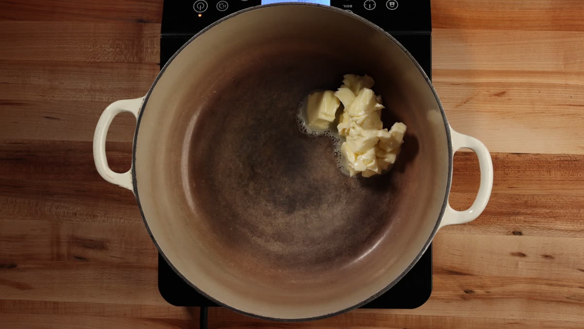 Pieces of butter starting to melt in an empty Dutch oven on an induction burner, seen from above