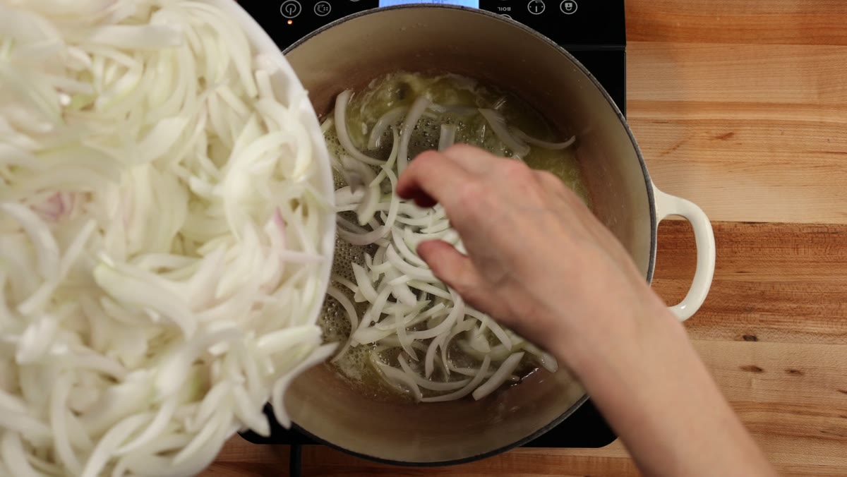 Sliced raw onions being added by hand to the melted butter in the Dutch oven
