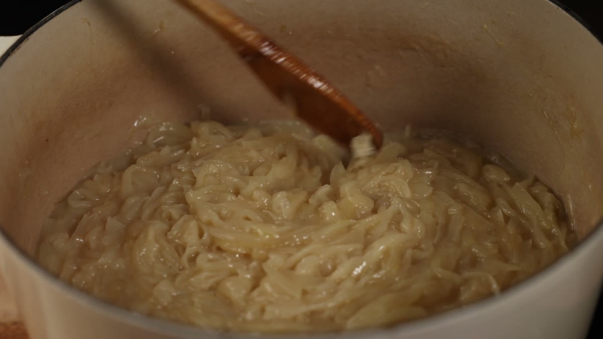 Soft, pale onions sitting in their own liquid in the pot, stirred with a wooden spoon