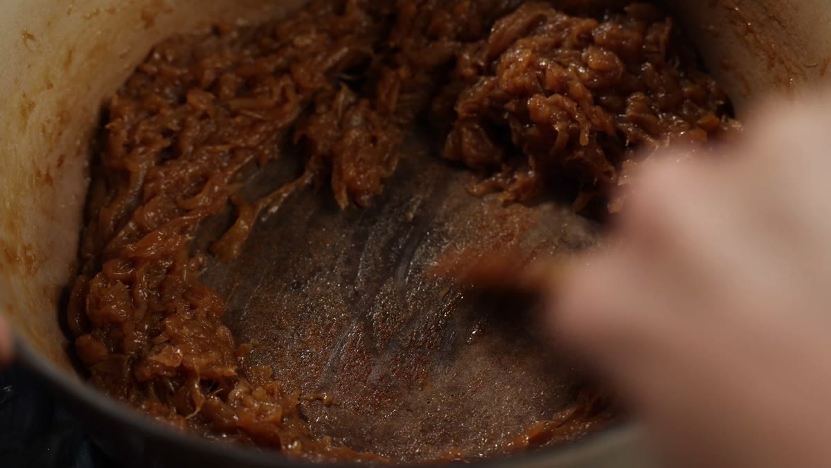 A wooden spoon scraping the brown bits off the bottom of the pot beside browned onions