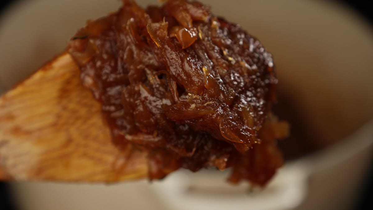 Dark brown caramelized onions, the color of a Tootsie Roll, heaped on a wooden spoon over the pot