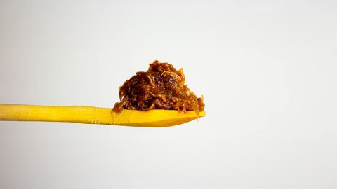 Caramelized onions piled on a yellow wooden spoon against a plain light background
