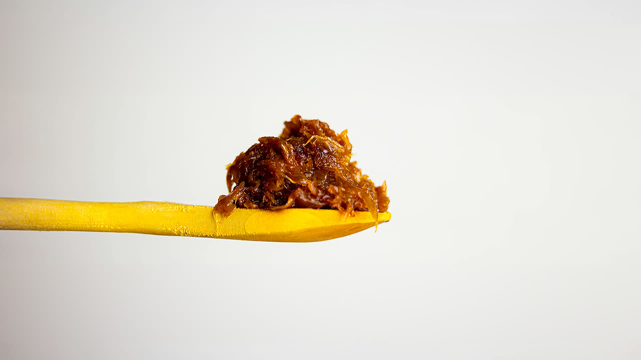 Caramelized onions piled on a yellow wooden spoon against a plain light background
