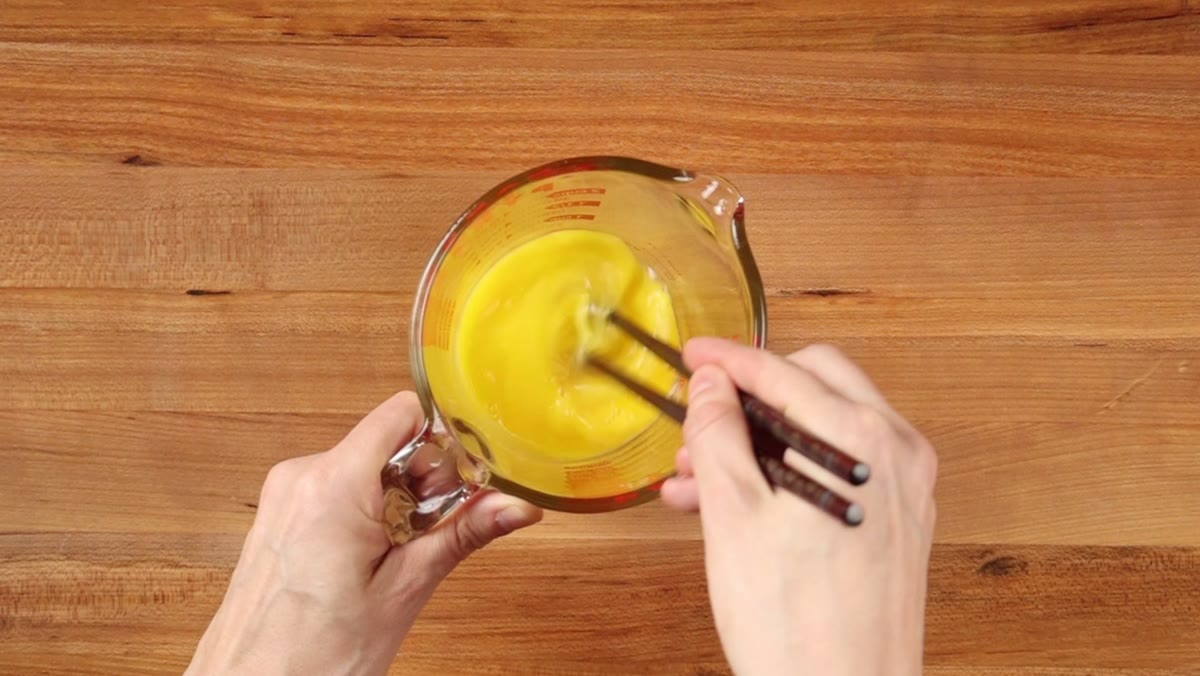 Two eggs being beaten with chopsticks in a glass measuring cup