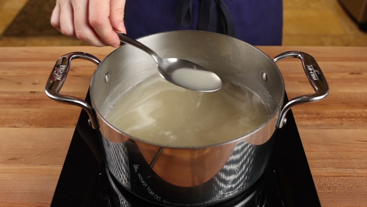 A spoon lifting broth thickened with cornstarch out of a steel pot