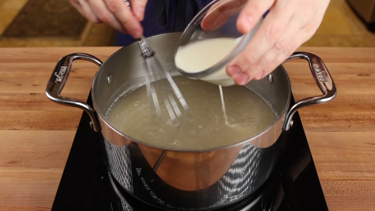 Cornstarch slurry being drizzled into the broth while a whisk stirs the pot
