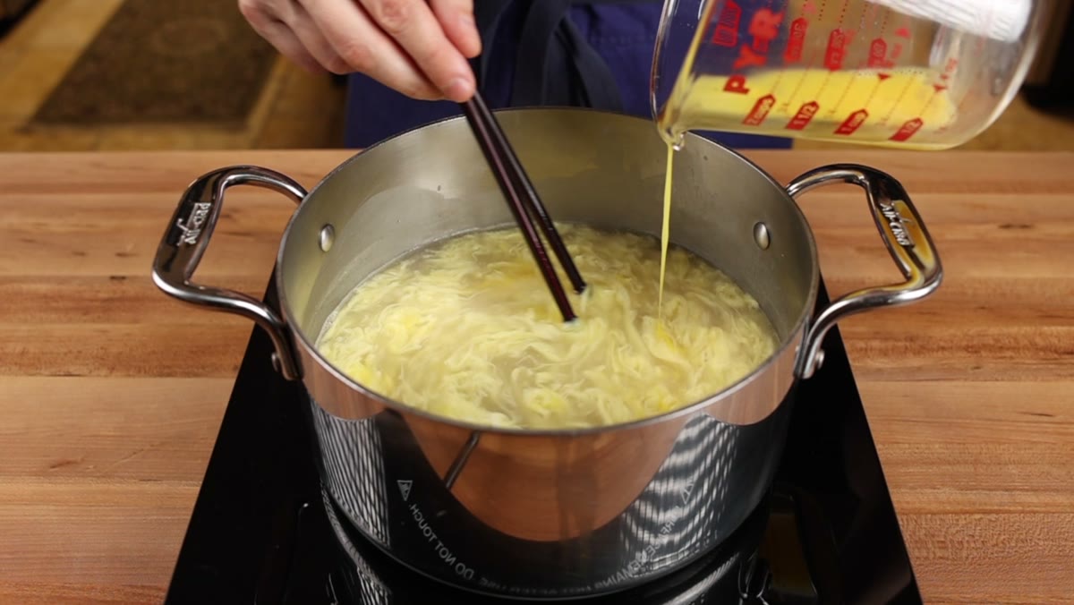 Wispy egg ribbons forming in the broth as more egg is poured in and stirred with chopsticks