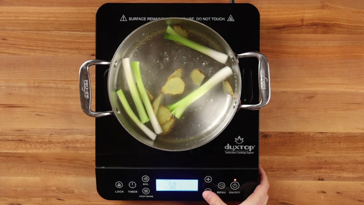 Sliced ginger and green onion bottoms steeping in a pot of water, seen from above