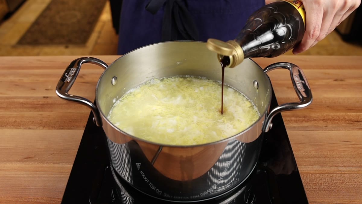 Chinese black vinegar being poured from a bottle into a pot of egg drop soup