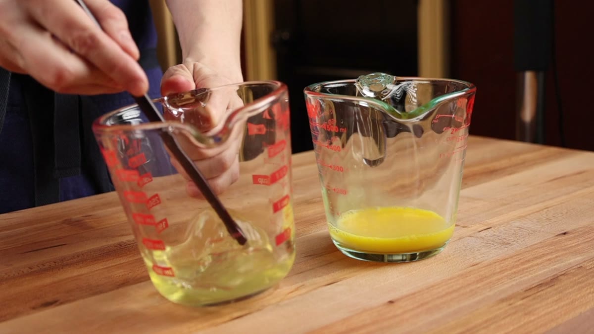 Egg whites being beaten with chopsticks in a measuring cup beside a cup of beaten yolks