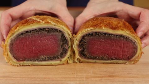 Gordon Ramsay-style beef Wellington cut in half and held up close, showing the medium-rare filet inside the mushrooms, crepe and golden puff pastry