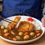 Japanese curry with carrots and whole potatoes beside white rice, topped with a sliced pork katsu cutlet
