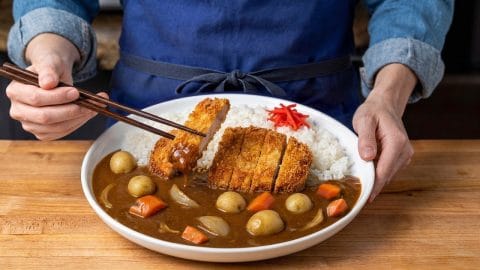 Japanese curry with carrots and whole potatoes beside white rice, topped with a sliced pork katsu cutlet