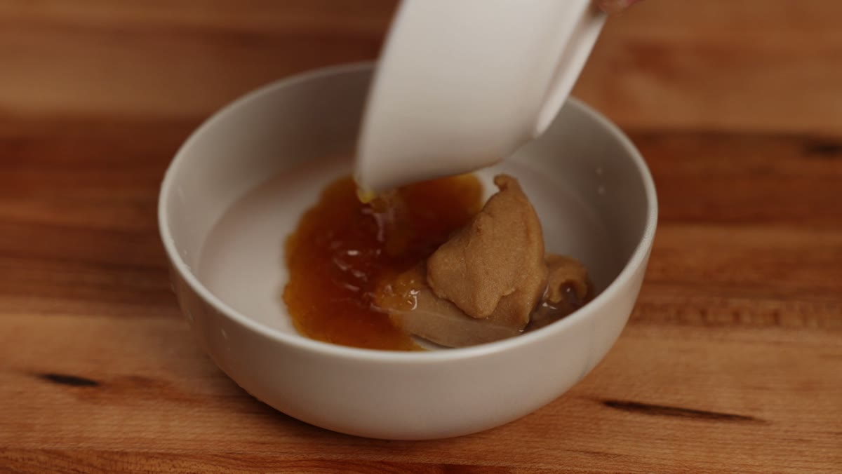 Fruit jam being poured into a white bowl of water and miso paste