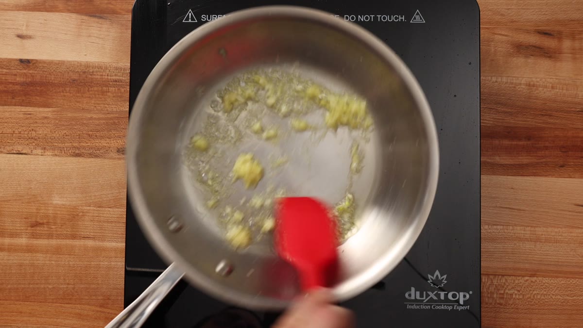 Stirring grated garlic and ginger in hot oil with a red spatula