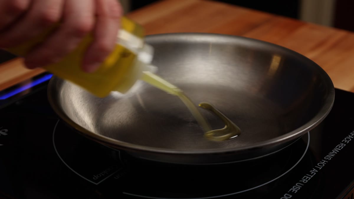 Oil being poured into a small stainless steel frying pan on an induction burner