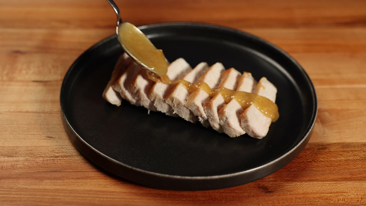 Spooning miso sauce over a sliced pork chop on a black plate