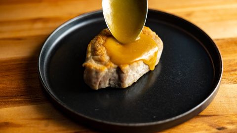 A spoonful of golden miso sauce poured over a pork chop on a black plate
