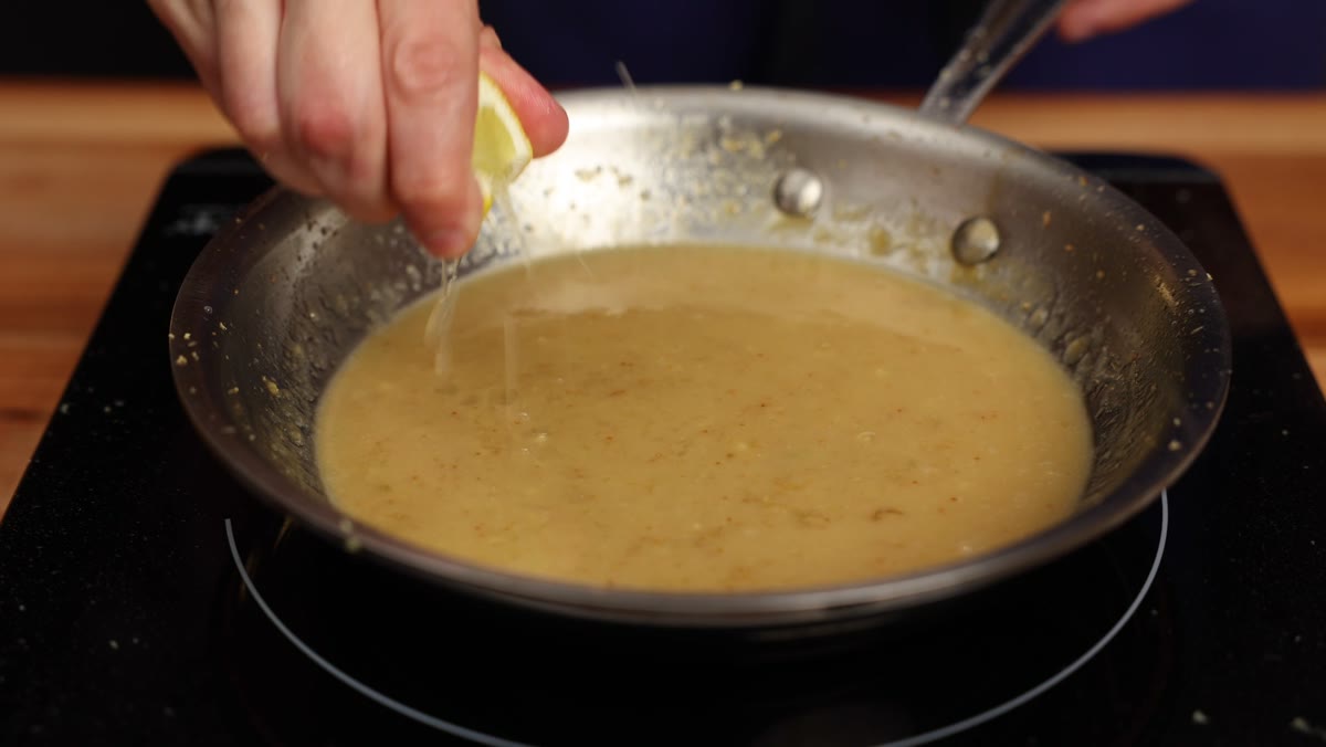 Squeezing a lemon wedge over the miso sauce in the pan