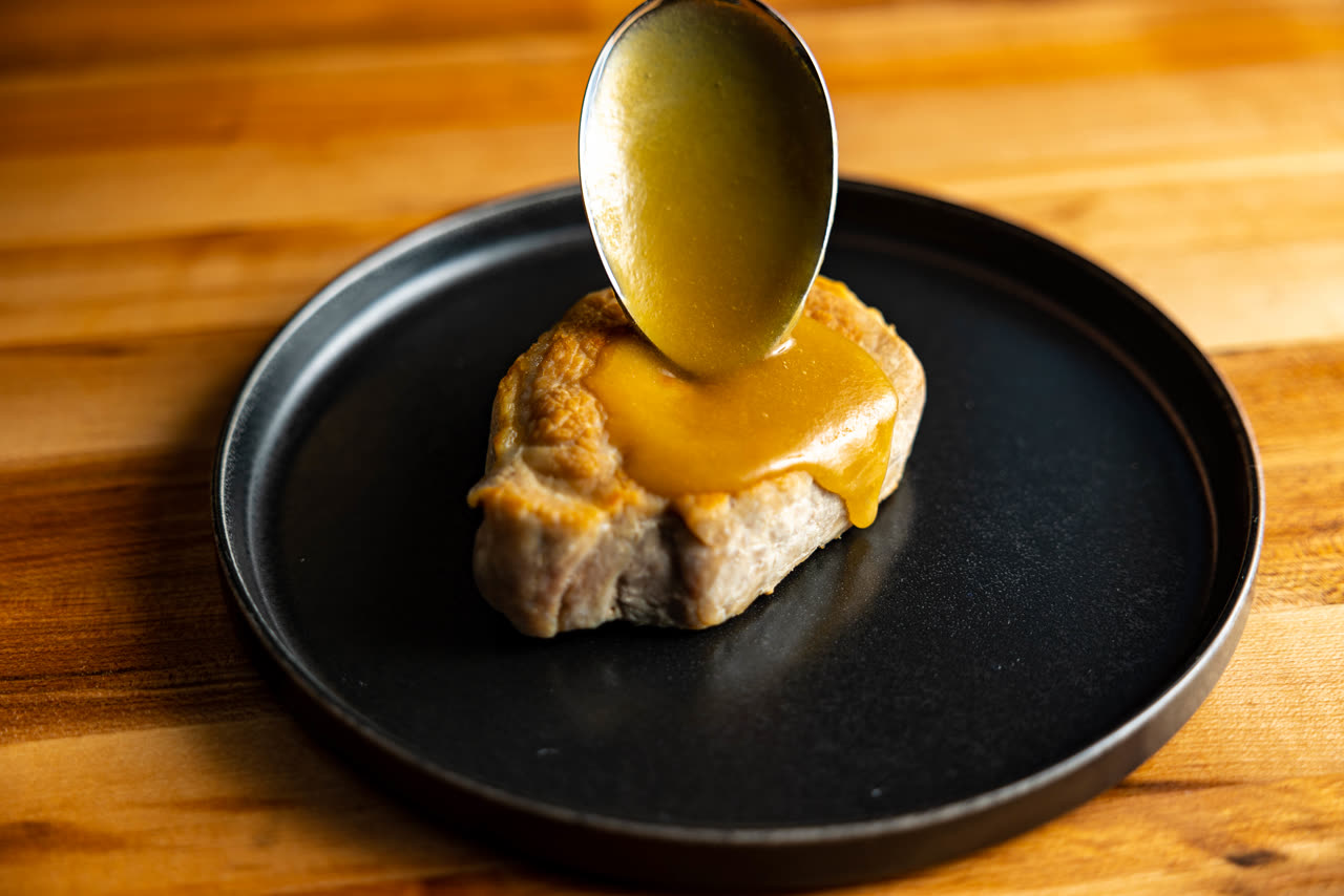 Miso sauce being spooned over a seared pork chop on a black plate