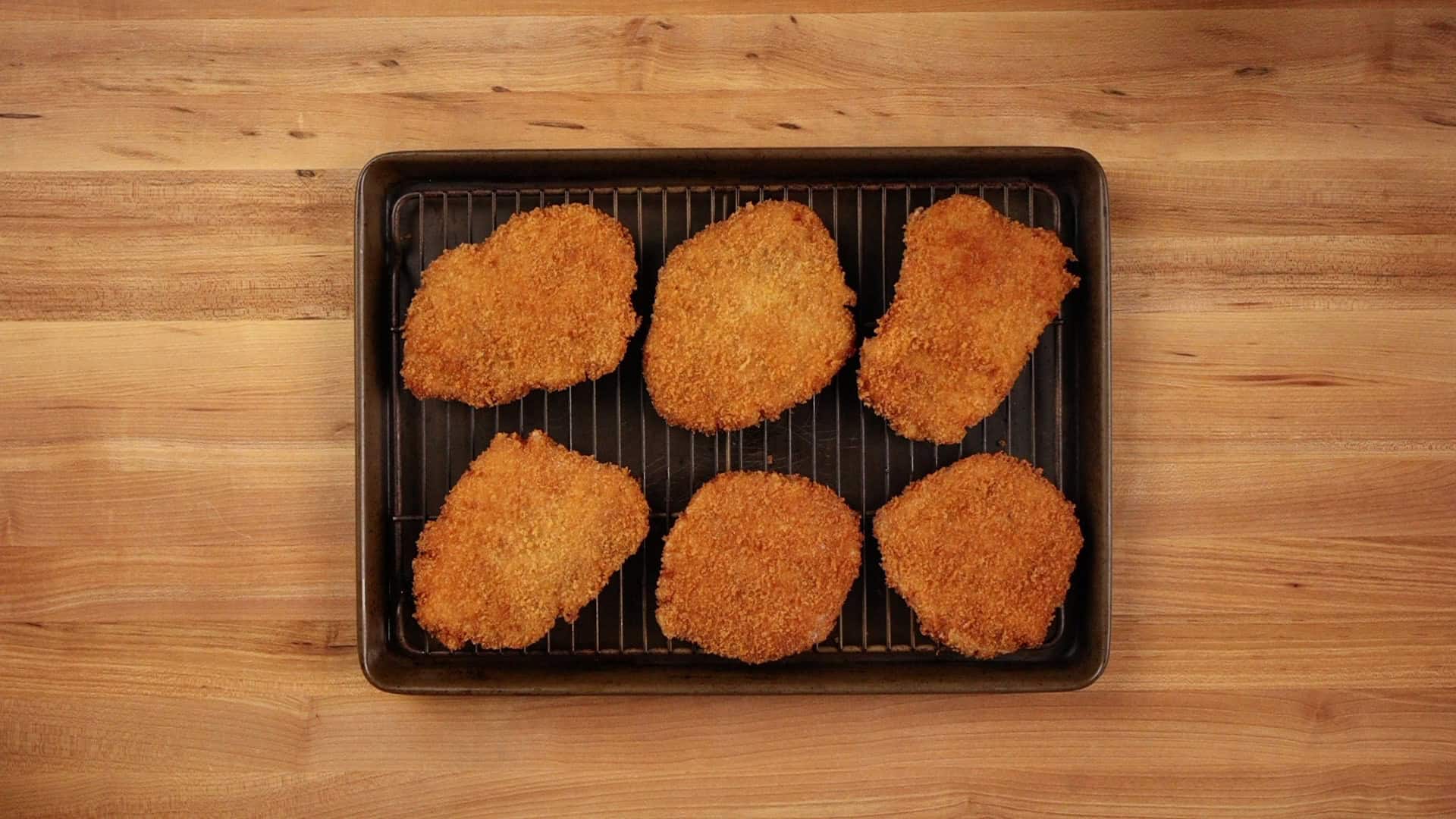 Six golden brown pork katsu cutlets resting on a wire rack